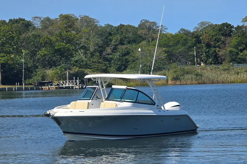 Slide: The Image of 2020 Pursuit DC 235 Dual Console boat cruising on a serene lake with houses in the background. - 3