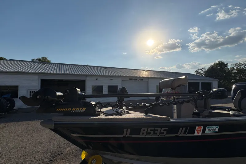 Slide: The Image of 2004 Lund 1800 Explorer SS boat with Minn Kota motor, parked outside a showroom under a sunny sky. - 7