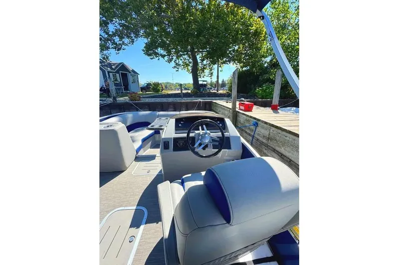 Slide: The Image of 2022 Bennington 23 LTFB boat interior with steering wheel and seating, docked by a wooden pier. - 19