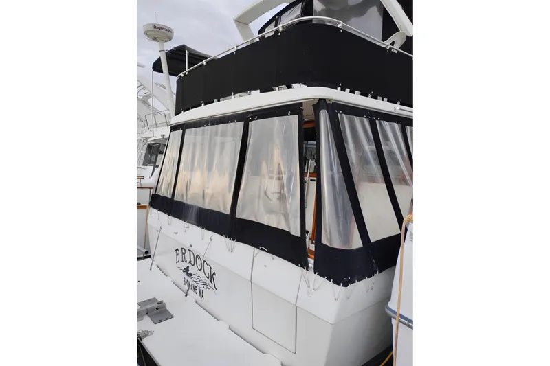 Slide: The Image of 1990 Bayliner 3888 Motoryacht with black canvas enclosure, docked in marina. - 3