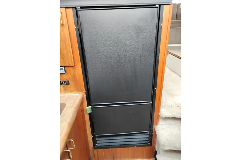 Slide: The Image of 1990 Bayliner 3888 Motoryacht interior with black refrigerator and wooden cabinetry. - 30