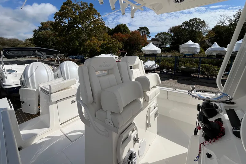 Slide: The Image of 2023 Regulator 28 boat interior with white seating and dual engines, docked outdoors. - 28