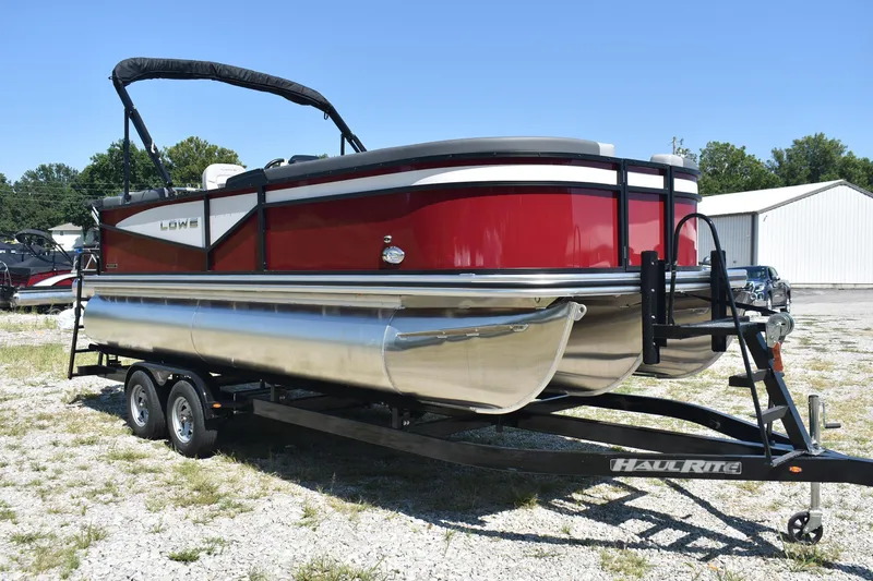 Slide: The Image of 2025 Lowe LS 210 WT pontoon boat on trailer, red and silver design, parked outdoors. - 5