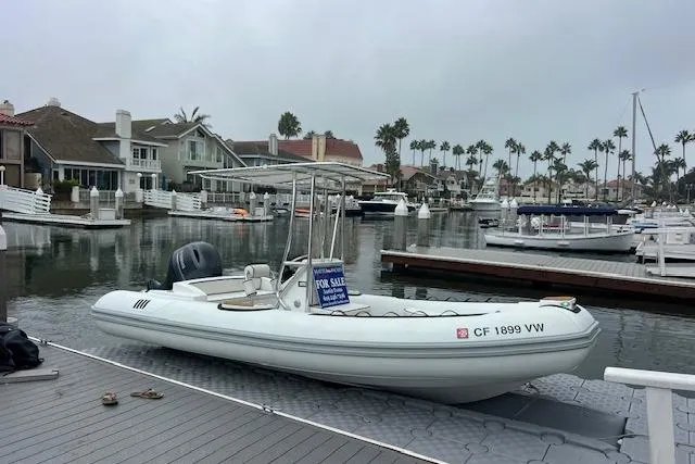 Slide: The Image of 2023 Novurania Como 18 boat docked, for sale sign, waterfront homes in background. - 2
