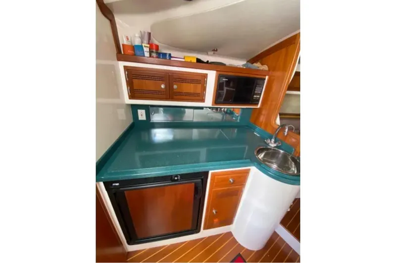 Slide: The Image of 1996 Cabo 31 Express boat kitchen with teal countertop, sink, microwave, and wooden cabinets. - 12