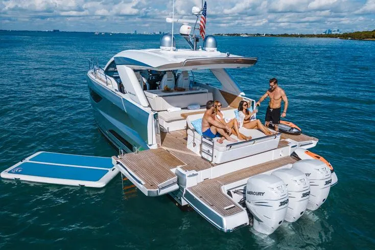 Slide: The Image of 2024 Jeanneau DB43 yacht cruising on a sunny day near palm-lined waterfront homes. - 2