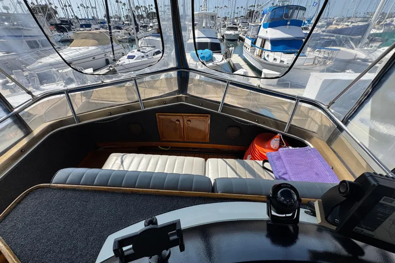 Slide: The Image of 1985 Carver 3607 Aft Cabin Motor Yacht helm with marina view, featuring seating and navigation equipment. - 29