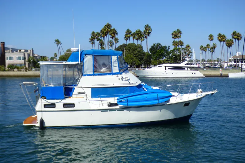 Slide: The Image of 1985 Carver 3607 Aft Cabin Motor Yacht on calm water, blue canopy, palm trees in background. - 4