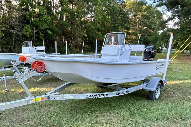 Slide: The Image of 2025 Coastal Skiff 171 boat on trailer, parked on grass with trees in background. - 10