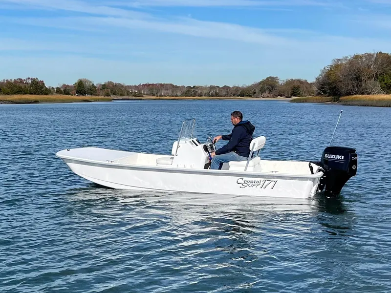 Slide: The Image of 2025 Coastal Skiff 171 boat on calm water with driver, featuring Suzuki outboard motor. - 2