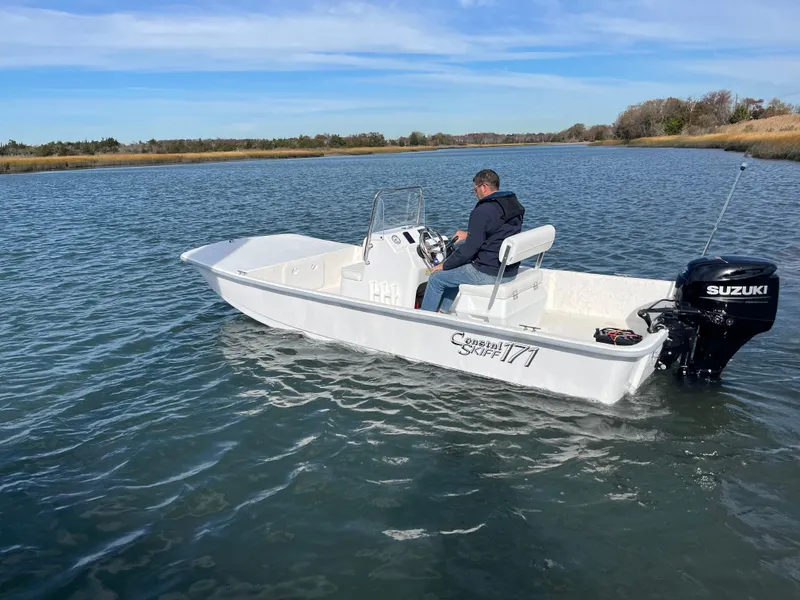 Slide: The Image of A person navigates a 2025 Coastal Skiff 171 boat on a calm lake. - 4