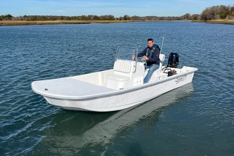 Slide: The Image of 2025 Coastal Skiff 171 boat on calm water with a person at the helm. - 6