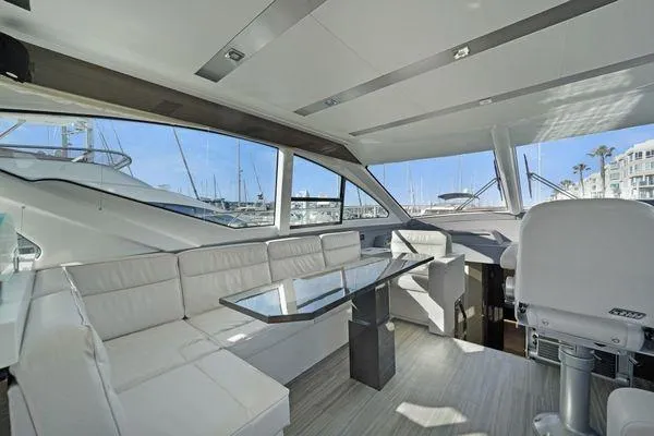 Slide: The Image of 2018 Cruisers Cantius yacht interior with white seating, glass table, and marina view. - 8
