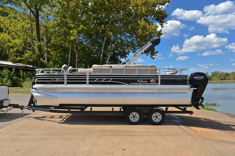 Slide: The Image of 2023 Sun Tracker Fishin' Barge 20 DLX pontoon boat on trailer by a lake. - 11