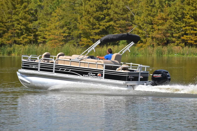 Slide: The Image of 2023 Sun Tracker Fishin' Barge 20 DLX pontoon boat cruising on a serene lake. - 4