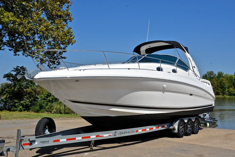 Slide: The Image of 2003 Sea Ray 320 Sundancer boat on trailer, parked near a lake under clear blue sky. - 13