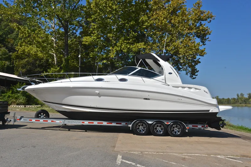 Slide: The Image of 2003 Sea Ray 320 Sundancer boat on trailer by a lake, surrounded by trees. - 16