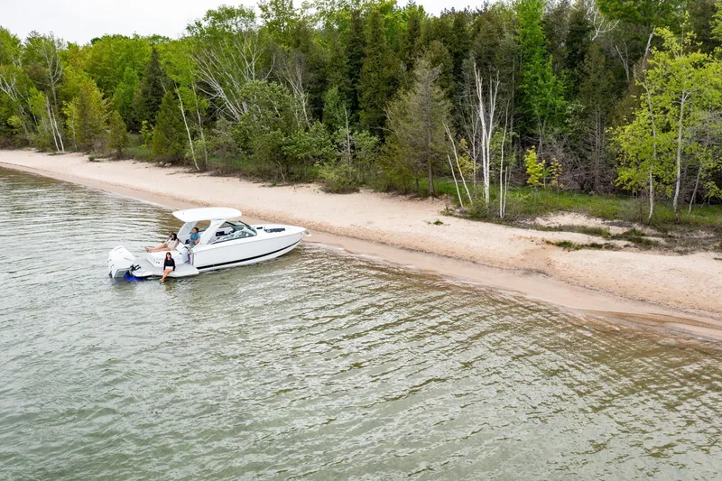 Slide: The Image of 2026 Four Winns H9 OB boat near a sandy beach with lush green trees. - 5