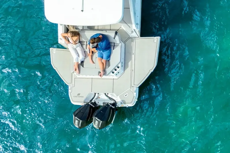 Slide: The Image of 2026 Four Winns H9 OB boat with two people relaxing on deck, surrounded by clear blue water. - 9