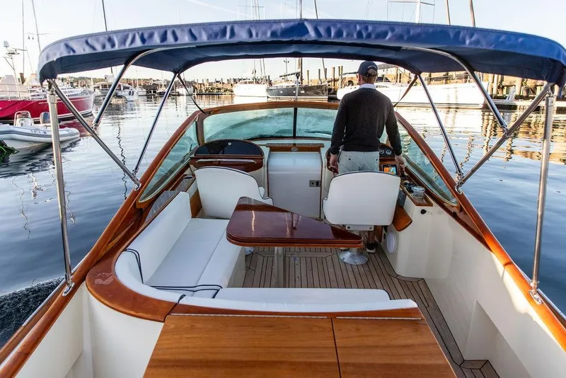 Slide: The Image of 2005 Hinckley Talaria 29R boat interior with wooden accents and seating, docked in a marina. - 11
