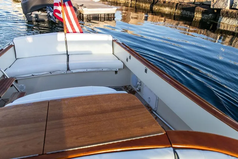 Slide: The Image of 2005 Hinckley Talaria 29R boat interior with wooden table and white seating, docked by calm water. - 13