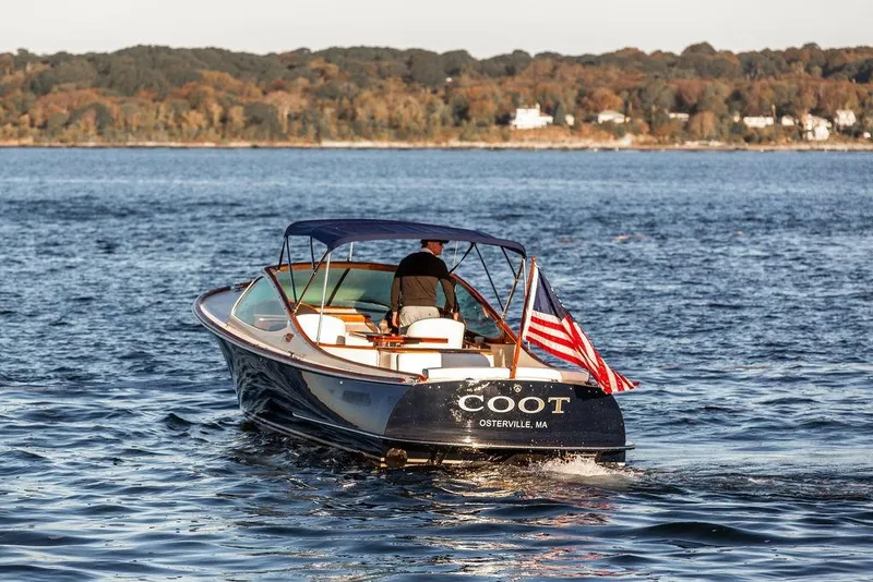 Slide: The Image of 2005 Hinckley Talaria 29R boat cruising on water with American flag, scenic background. - 2