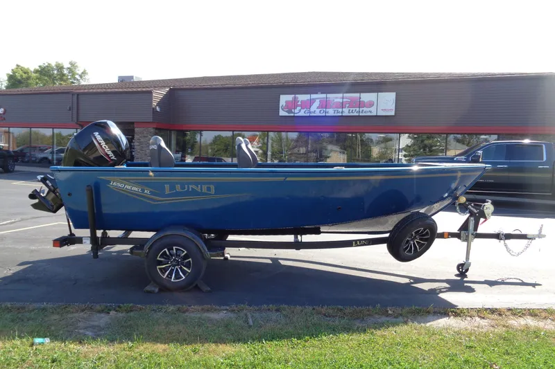 The Image of 2026 Lund 1650 Rebel Tiller boat on trailer, parked outside a dealership. - 1