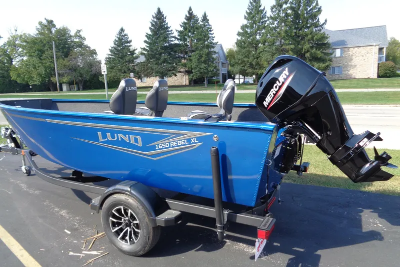 Slide: The Image of 2026 Lund 1650 Rebel Tiller boat with Mercury engine, parked outdoors. - 2