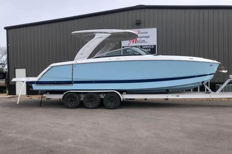 The Image of 2025 Four Winns H9 boat on trailer, light blue hull, parked outside marine service building. - 0