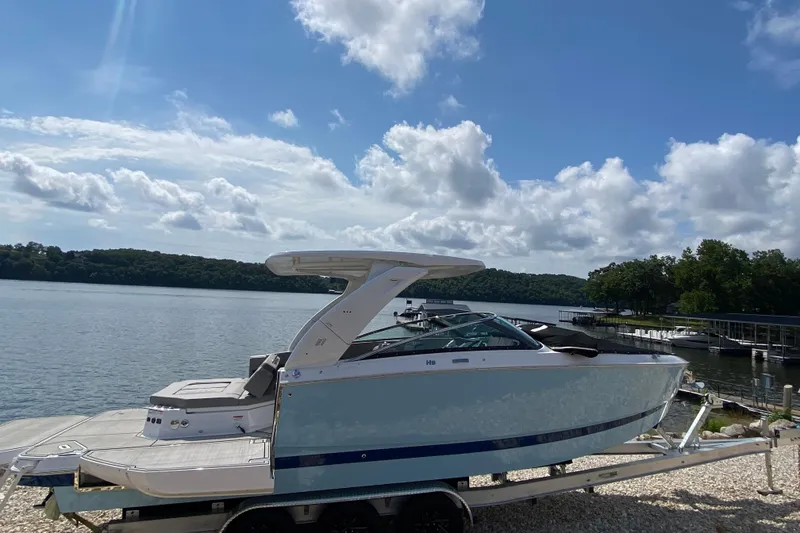 Slide: The Image of 2025 Four Winns H9 boat on trailer by scenic lake under cloudy sky. - 2