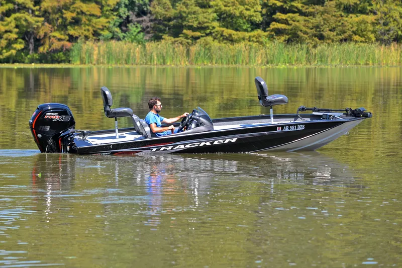 Slide: The Image of 2023 Bass Tracker PRO TEAM 190 boat on a calm lake with lush greenery. - 7