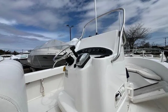 Slide: The Image of 2005 Boston Whaler 190 Nantucket boat console with steering wheel, docked under cloudy sky. - 10