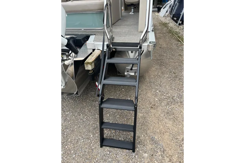 Slide: The Image of 2026 Tahoe 25 LTZ Entertainer boat with foldable boarding ladder on gravel surface. - 10