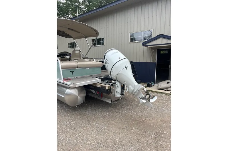 Slide: The Image of 2026 Tahoe 25 LTZ Entertainer pontoon boat with outboard motor, parked near a building. - 12