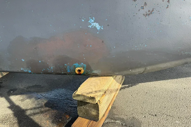 Slide: The Image of 1988 Island Packet 27 hull with visible wear and rust, supported on wooden blocks. - 6