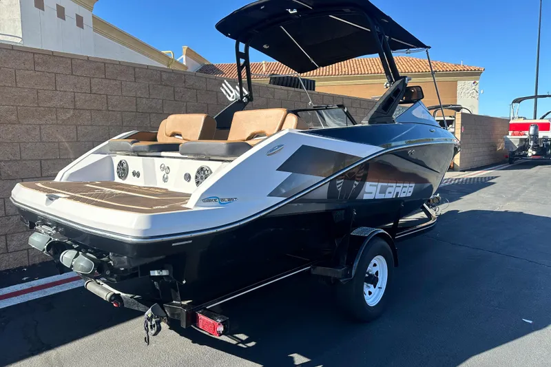 Slide: The Image of 2019 Scarab 215 Wake ID boat on trailer, parked outdoors with mountain backdrop. - 2