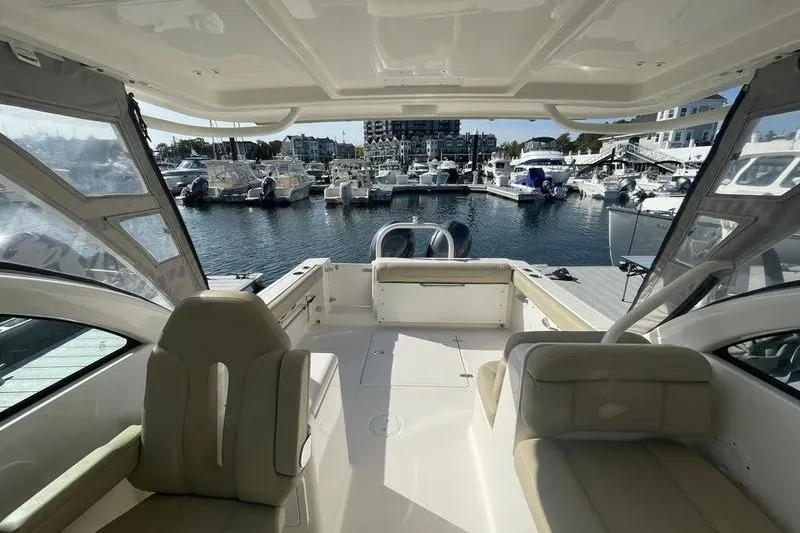 Slide: The Image of 2016 Pursuit DC 265 Dual Console boat interior at marina, showcasing seating and docked boats. - 16