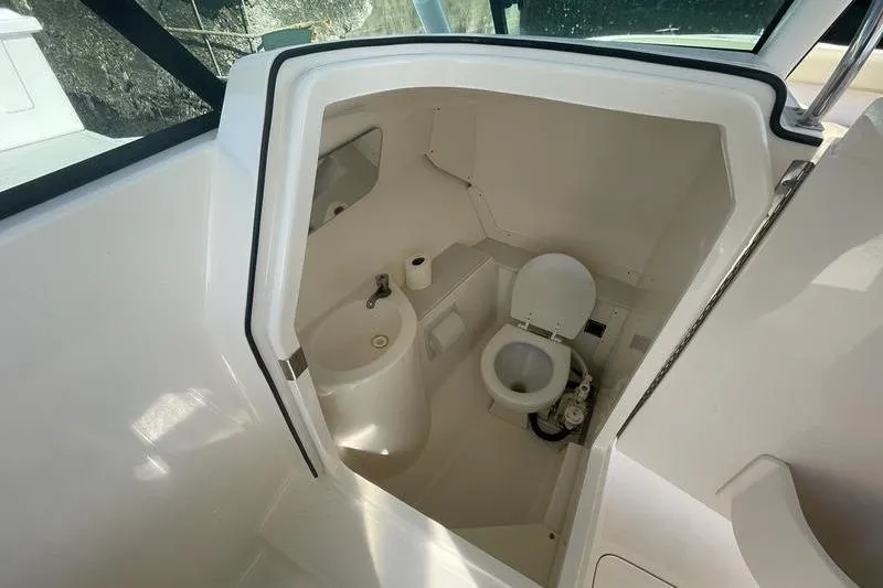 Slide: The Image of Interior of 2016 Pursuit DC 265 boat showing compact bathroom with toilet and sink. - 17