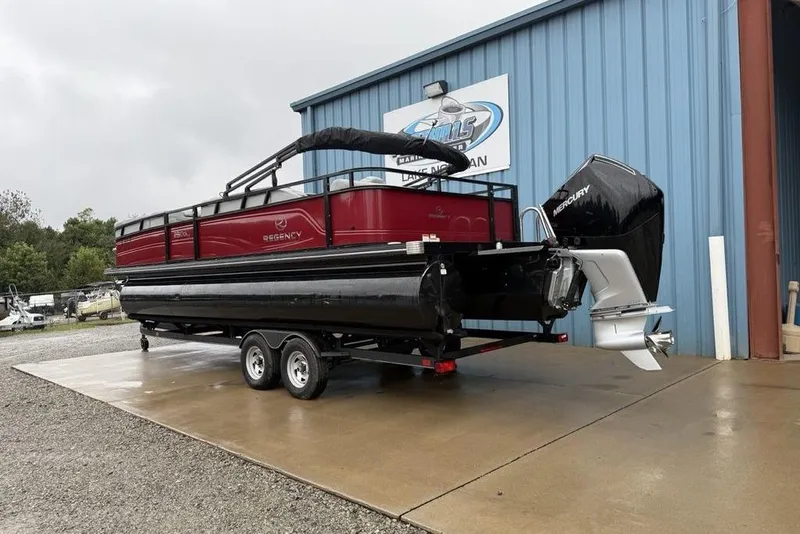 Slide: The Image of 2023 Regency 250 DL3 pontoon boat with Mercury engine, parked outside a blue building. - 34