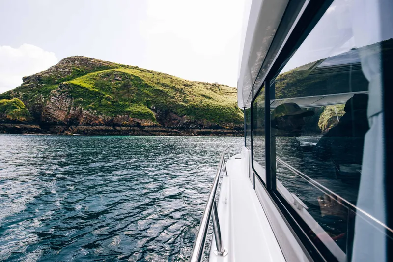 Slide: The Image of 2026 Jeanneau NC 895 Sport Series 2 cruising near a lush, rocky island. - 12