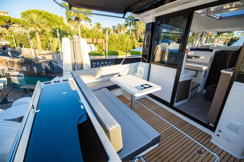 Slide: The Image of 2026 Jeanneau NC 895 Sport Series 2 boat interior with seating and table, docked near lush greenery. - 16