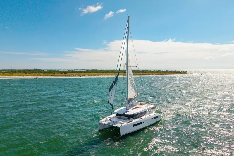 Slide: The Image of 2021 Leopard 45 catamaran sailing near a scenic coastline under a clear blue sky. - 114