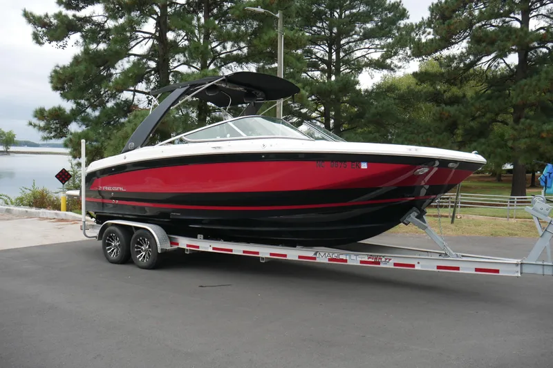 Slide: The Image of 2019 Regal 26 FasDeck boat on trailer, parked near a lake with trees in the background. - 34