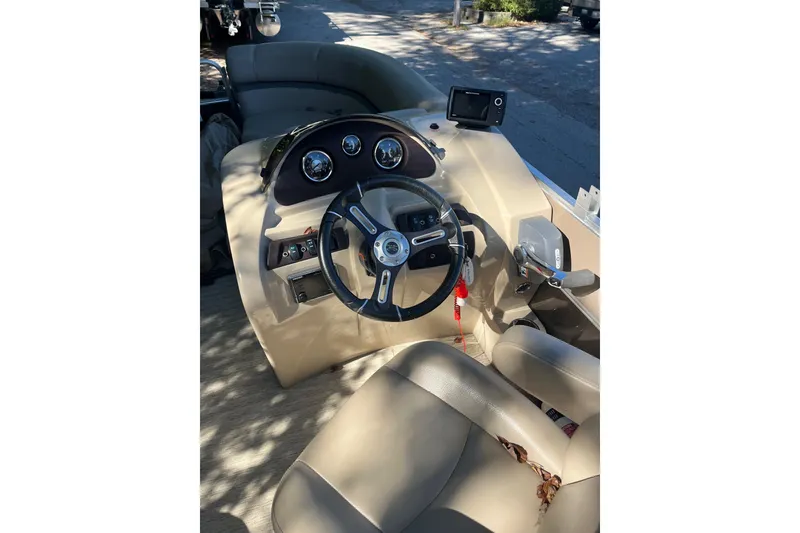 Slide: The Image of 2018 Berkshire 22 Quad Bench Tritoon steering console with beige seating and dashboard controls. - 1
