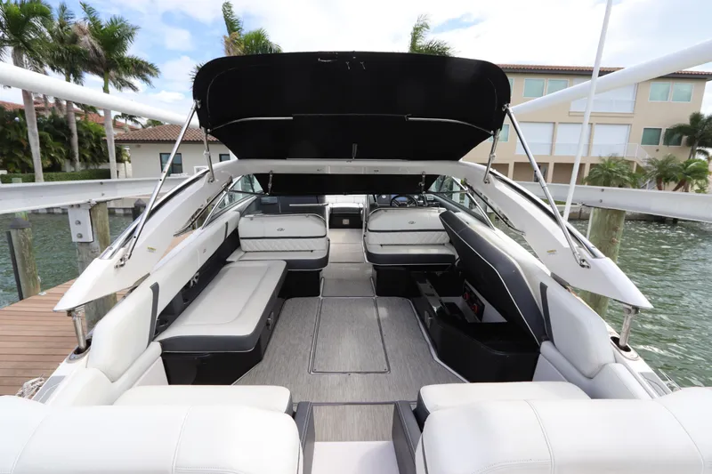 Slide: The Image of 2018 Regal 29 OBX boat interior with spacious seating and canopy, docked by waterfront homes. - 13