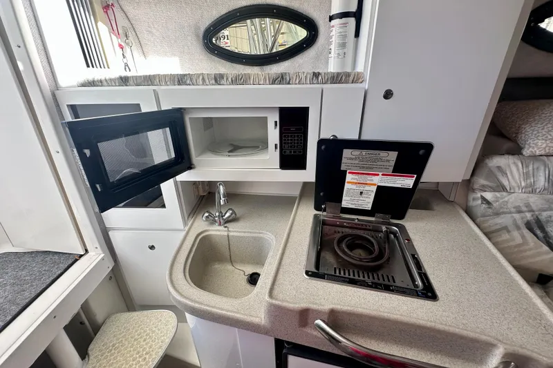 Slide: The Image of 2001 Wellcraft 290 Coastal boat interior with kitchenette, featuring sink, stove, and microwave. - 14