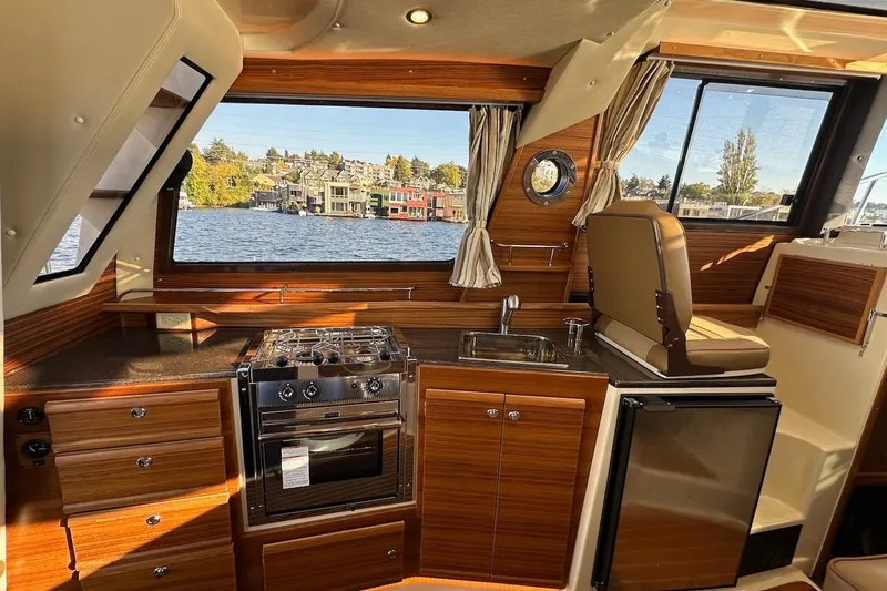Slide: The Image of 2025 Ranger Tugs R-29 CB interior with kitchen, stove, sink, and scenic water view. - 32