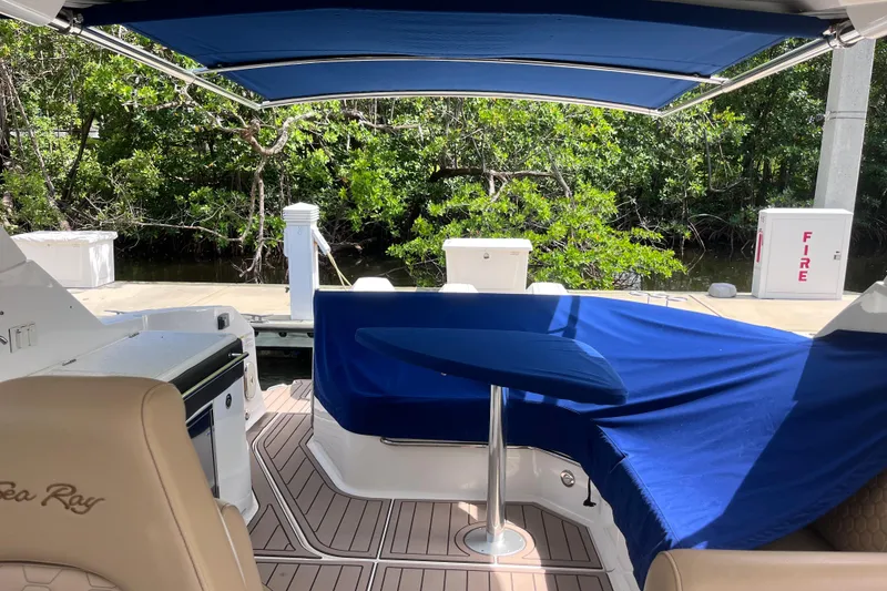 Slide: The Image of 2020 Sea Ray Sundancer 320 Outboard interior with blue canopy and seating, docked near lush greenery. - 15