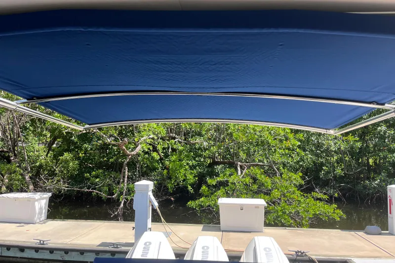 Slide: The Image of 2020 Sea Ray Sundancer 320 Outboard with blue canopy docked near lush greenery. - 16