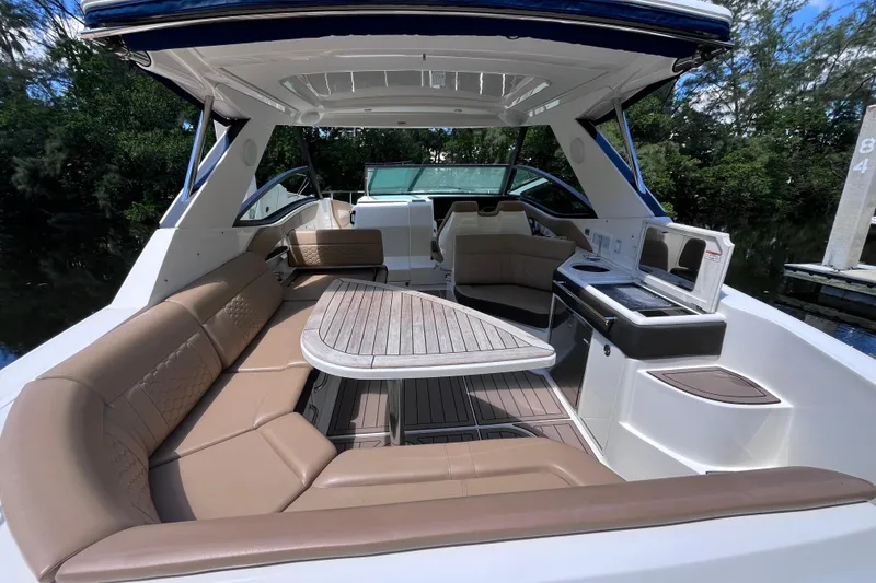Slide: The Image of 2020 Sea Ray Sundancer 320 Outboard interior with seating and kitchenette, docked by lush greenery. - 44